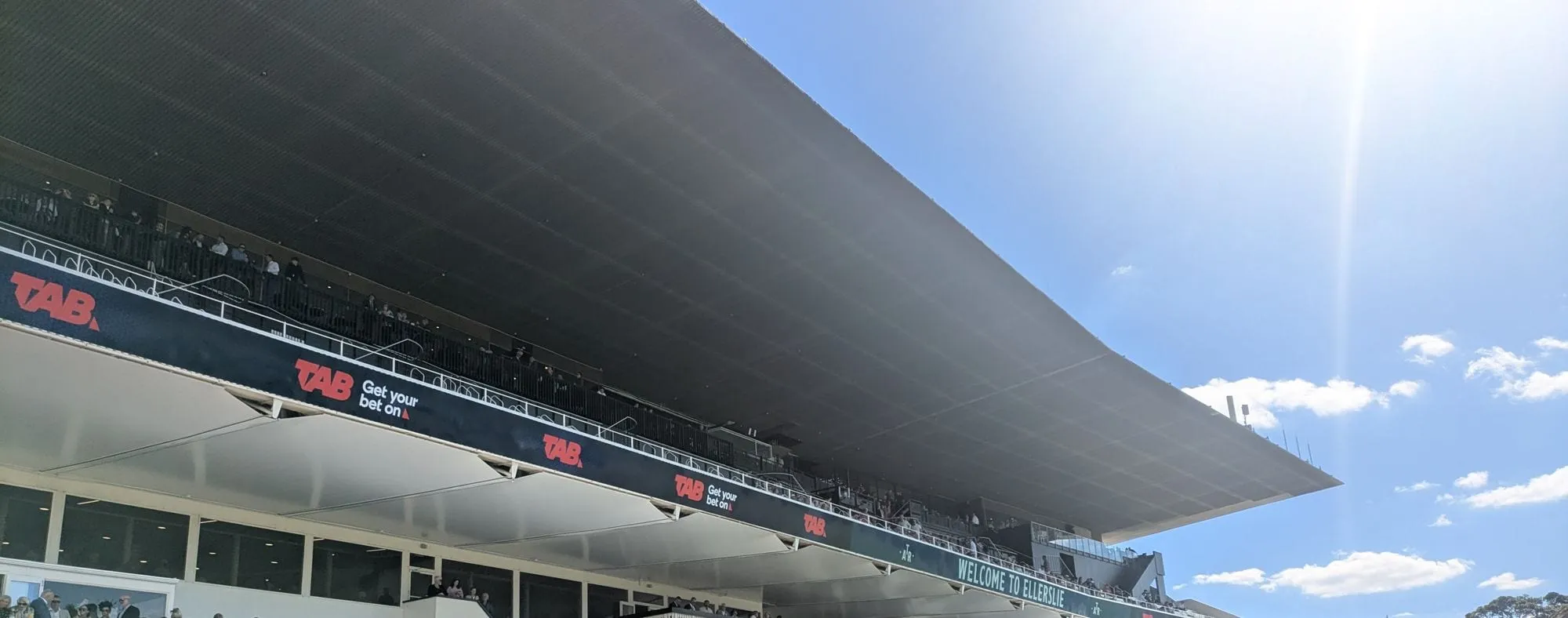 エラズリー競馬場のメインスタンド。大きな屋根の下に座席が並び、上の階にも観客が見える
